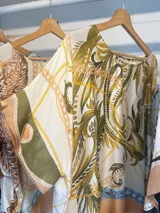 Blusa de satén con estampado de cadenas y hojas en tonos blanco, marrón y negro. Tiene corte amplio, mangas cortas y cuello redondo. Se ajusta a la cintura con un cinturón elástico negro con hebilla dorada.