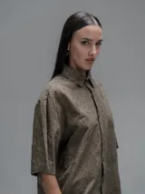 Camisa de manga corta color verde militar, con cuello clásico y cierre de botones frontales. Presenta un estampado floral en relieve.