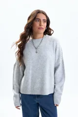 Buzo de punto gris de corte holgado, con cuello redondo y detalle de tachas metálicas aplicadas a lo largo de la sisa y la parte superior de las mangas.