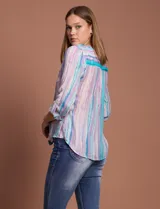 Blusa de gasa con estampado de rayas verticales en tonos celestes, violetas y blancos. Presenta cuello mao con escote en V, cierre frontal con botones, bolsillo aplicado en el pecho y mangas largas con presilla para regular el largo. El diseño incluye un nudo en la parte inferior delantera.