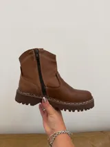 Bota de caña baja confeccionada en cuero vacuno encerado color marrón chocolate. Presenta costuras a la vista en tono contrastante, diseño de estilo western y suela track cosida a tono.