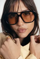 Lentes de sol con armazón de policarbonato negro y cristales tonalidad ámbar, con diseño de puente doble estilo aviador.