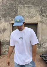 Remera blanca de algodón con corte boxy y parche bordado con la palabra "Brokers" en óvalo azul y verde.