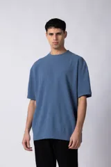 Remera de corte oversized en color marrón, confeccionada en tejido de algodón con textura de micropanal. Presenta cuello redondo con detalle de costura en forma de X y mangas cortas de estilo caído.