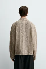 Sobrecamisa de hombre color beige, confeccionada en tejido de crochet con estructura abierta, cuello solapa, manga larga y cierre frontal de botones.