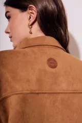 Sobrecamisa negra de estilo shacket, confeccionada en tejido de gamuza sintética. Presenta cuello camisero, cierre frontal de botones y dos bolsillos de parche con solapa en el pecho. El calce es oversize y las mangas son largas.