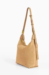 Cartera tipo hobo de cuero color camel, con diseño holgado y cierre superior. Presenta un detalle metálico en la parte superior y el logo de la marca grabado en el frente.