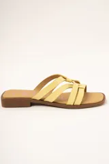 Sandalias planas de cuero color amarillo, con múltiples tiras finas entrelazadas en el empeine, suela baja y plantilla marrón.