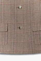 Blazer corto de corte estructurado con cuello solapa, manga larga y hombreras. Presenta cierre frontal con botones metálicos y dos bolsillos delanteros de plastrón con solapa. Diseño con estampado de cuadros tipo príncipe de gales.