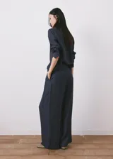 Pantalón azul marino de tiro alto con sutiles rayas diplomáticas blancas, de corte amplio y fluido con bolsillos laterales.