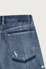 Bermuda baggy fit confeccionada en denim de algodón con lavado azul y efecto rotos en toda la prenda. Presenta diseño de cinco bolsillos, detalles de costuras en las perneras, bajo acabado irregular y cierre frontal con cremallera y botón.