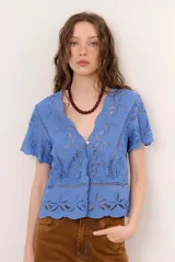 Camisa azul de manga corta confeccionada en tejido broderie con diseño calado y floral. Cuenta con escote en V y cierre frontal de botones.