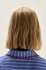 Camisa de corte holgado con diseño de rayas verticales en azul y blanco. Presenta cuello clásico y cartera frontal con detalles bordados en hilo rojo. Incluye un pequeño bordado de estrellas en el pecho y mangas largas con puños estructurados.