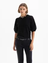 Top de punto negro con mangas cortas abullonadas que presentan detalles de flecos texturizados. El diseño cuenta con cuello redondo y un corte ajustado a la cadera.