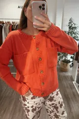 Saco tejido de punto color naranja, con cuello redondo, cierre frontal de botones y dos bolsillos frontales tipo parche. Presenta puños y ruedo acanalados.
