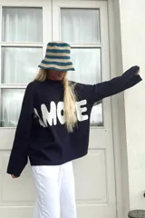 Sweater de punto negro con cuello redondo y mangas largas, presenta la palabra 'AMORE' estampada en letras grandes de color blanco en el frente.