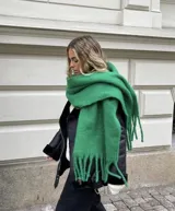 Bufanda de tejido suave y esponjoso en color verde intenso, con diseño de flecos largos en los extremos.