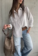 Camisa de corte oversize, con diseño a rayas verticales marrón sobre fondo blanco, manga larga, cuello camisero y bolsillos frontales.