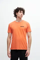 Remera naranja de algodón con cuello redondo y manga corta. Estampa pequeña con la palabra "UNIFORM" en el frente.