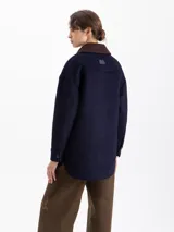 Chaqueta reversible de corte recto. Un lado confeccionado en paño azul marino con cuello de corderoy color chocolate, bolsillos frontales y cierre de botones. El lado interno está realizado en nylon color verde militar.