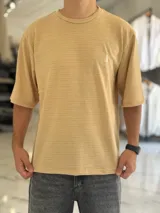 Remera oversize de tejido texturizado color tostado, con mangas cortas y cuello redondo. Presenta un pequeño bordado al tono en el lado izquierdo del pecho.