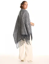 Ruana de tejido tipo tweed en tonos azul y gris con destellos de lurex. Presenta un diseño abierto con terminaciones desmechadas y flecos en todo el borde inferior.