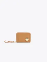 Billetera compacta de cuero vacuno color suela, con aplique metálico dorado en forma de vaquita de San Antonio en el frente. Incluye correa de muñeca y cierre perimetral.