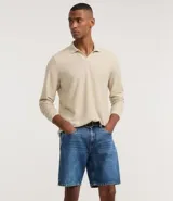 Bermuda de hombre confeccionada en denim de algodón, color azul medio, con tiro medio y corte recto. Presenta cierre de botón y cremallera, bolsillos delanteros y traseros, y etiqueta aplicada en la parte trasera de la cintura.