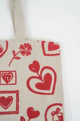 Bolso tote de tela con estampado de rayas verticales rosadas y blancas, laterales y asas en color beige. Presenta la palabra "BONJOUR" en verde en el centro y "INDIAN" en la parte inferior.