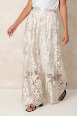 Pollera larga de tul con bordados florales en tono crema. Posee un forro interno opaco que llega hasta la rodilla, creando un efecto de transparencia en la parte inferior.