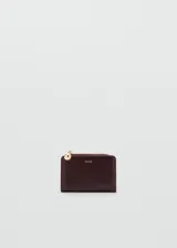 Billetera de poliuretano color bordó de la marca Mango, con diseño compacto, cierre de cremallera con tirador esférico dorado y logo estampado en el frente.