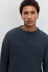 Sweater de tejido de punto acanalado en color marrón, con cuello redondo y ajuste holgado. Presenta un pequeño bordado distintivo en el pecho.