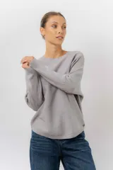 Buzo tejido de punto en color beige, con cuello redondo, mangas largas y silueta relajada con dobladillo irregular, siendo más largo en la parte trasera.