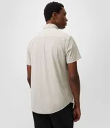 Camisa de manga corta color beige, con cuello camisero, cierre frontal de botones y diseño liso.