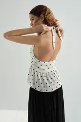 Top halter color blanco con estampado de lunares negros, escote en V pronunciado y detalle fruncido en la cintura con vuelo tipo peplum.
