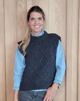 Chaleco de punto gris oscuro con diseño de trenzas y rombos en relieve, cuello redondo y terminaciones acanaladas.