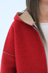 Tapado de paño rojo con capucha, cierre frontal y detalles en color beige en el interior, puños y bordes de los bolsillos. Presenta un corte recto y holgado.