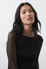 Vestido largo de manga larga confeccionado en tejido de malla transparente con sutil textura. Presenta un diseño entallado, cuello redondo y una silueta estilizada.