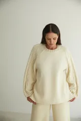 Buzo de lana fina sin teñir con cuello redondo y mangas raglán. Presenta un diseño de tejido de punto con dibujo de cables en las mangas y cuerpo liso.