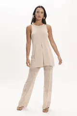 Pantalón de tejido de punto negro, corte ancho y tiro alto, con detalle de encaje calado en la parte inferior. Se lleva debajo de un vestido largo de encaje negro con tirantes finos y botones frontales.