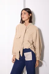 Camisa de tela afelpada color beige con nudo en el cuello, mangas abullonadas con lazos en los puños y bolsillos frontales con tapa.