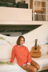 Buzo color naranja con cuello redondo, manga larga y un pequeño corazón bordado en el frente. La espalda presenta un bordado con el significado de "Munay" y un poema. Confeccionado en rústico de algodón.