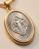 Collar de cadena de eslabones con baño de oro y dije ovalado colgante con relieve de San Benito en tono plateado y borde dorado.
