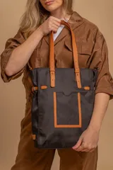 Bolso tipo tote bag de símil cuero color rosa pálido, con asas dobles y detalles de costura en color beige claro. Presenta un bolsillo frontal rectangular aplicado y herrajes metálicos.