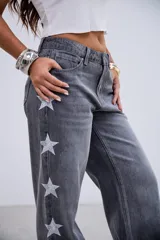 Jean de corte recto y tiro medio-bajo, color gris lavado, con detalle de estrellas bordadas a lo largo de los laterales externos de las piernas.