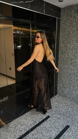 Vestido largo de encaje negro con cuello halter y espalda descubierta. Tiene un corte a la altura de la rodilla y un ruedo largo transparente.