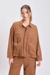 Chaqueta tipo camisa de lino color marrón, de corte holgado y manga larga. Presenta cuello camisero y cuatro bolsillos frontales con solapa.