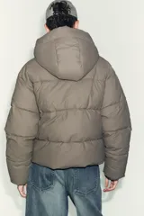 Campera puffer corta de tejido engomado resistente al viento, con aislamiento térmico. Presenta cuello subido con capucha, manga larga, bolsillos delanteros y bajo ajustable con stoppers laterales. Cierre frontal con cremallera termosellada y botones magnéticos.
