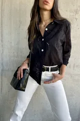 Camisa negra con bordado calado, corte recto y aberturas laterales.