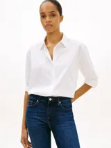 Camisa blanca de algodón orgánico con cuello camisero, cierre frontal de botones y manga larga ajustable con presilla. Cuenta con el logo de Tommy Hilfiger bordado sutilmente en el pecho.